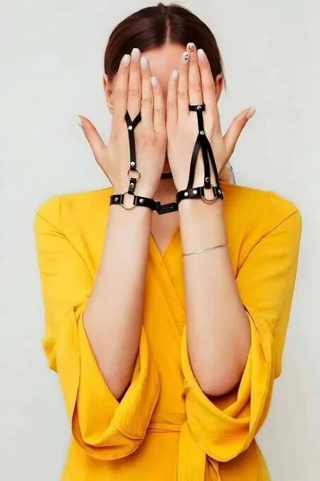 Black faux leather fingerless hand harness with silver O-ring hardware and wrist cuff worn on both hands over yellow dress