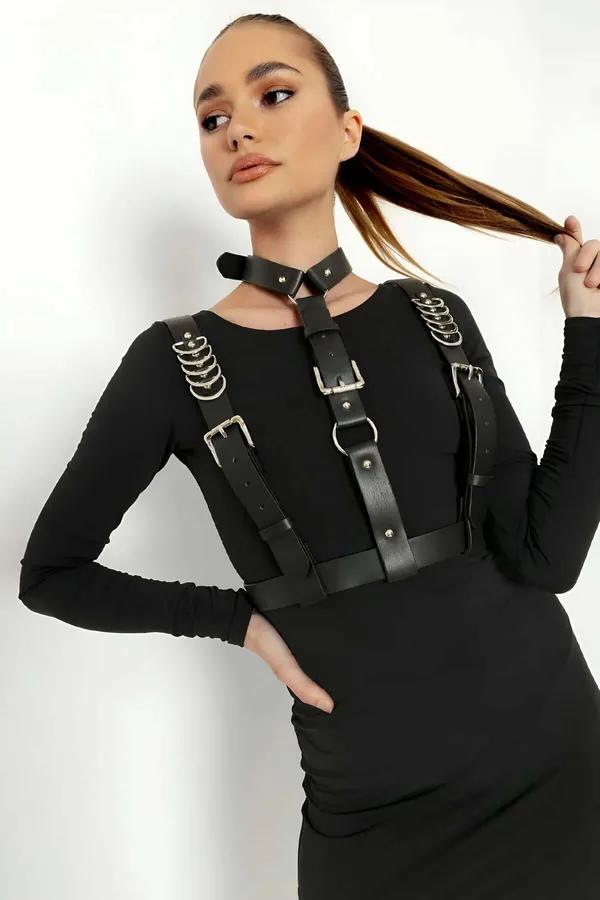 black faux leather chest harness with stacked silver O-rings and adjustable buckles worn over black dress