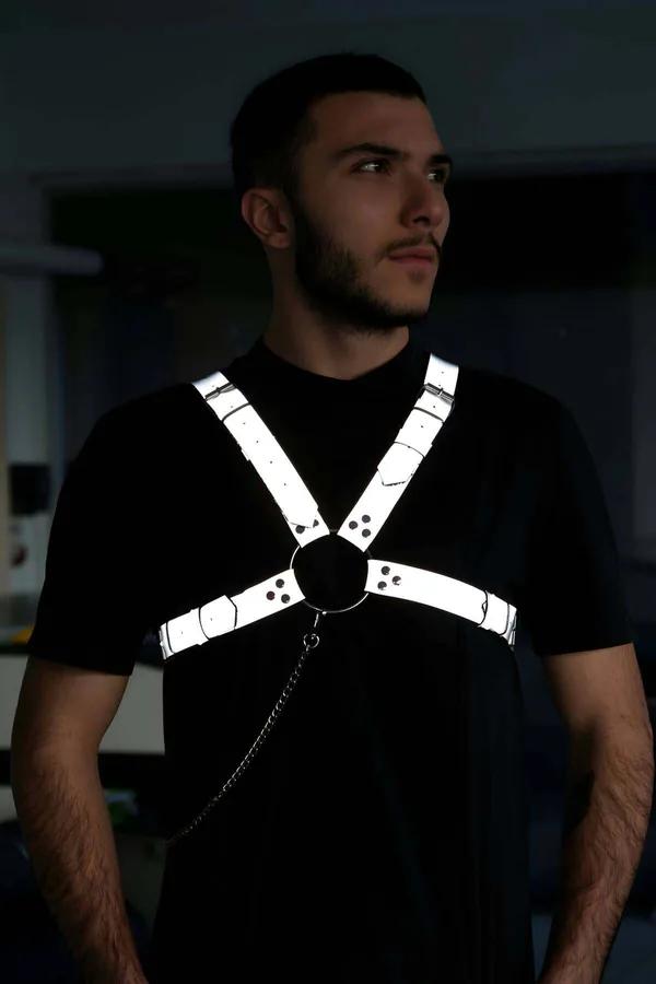 Reflective white chest harness with black O-ring center and chain detail worn by man over black t-shirt