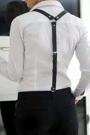 Black faux leather suspender harness worn over a white shirt, showing adjustable straps and silver hardware.