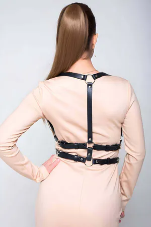 Black faux leather strappy chest harness with O-ring accent worn by model