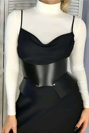 Sculpted black faux leather waist cincher belt with angular panels worn over a black cowl neck top and white turtleneck