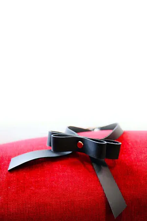 Black faux leather bow tie choker with dangles, worn around neck.