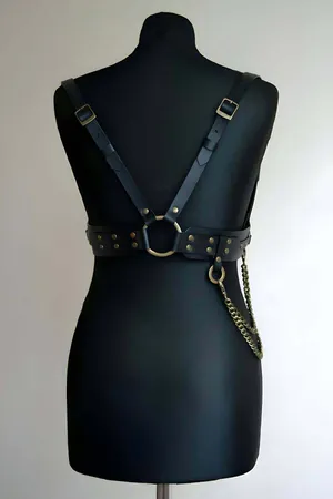 Black faux leather body harness with antique gold O-ring and decorative chain detail.