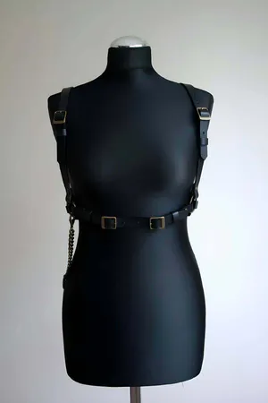 Black faux leather body harness with antique gold O-ring and decorative chain detail.