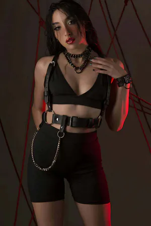 Black adjustable faux leather body harness with shoulder straps and detachable chain, worn by a model.
