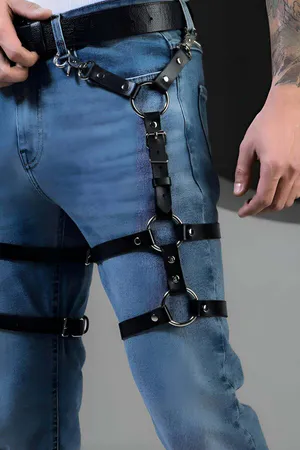 Adjustable black faux leather leg harness with silver O-rings attached to a belt