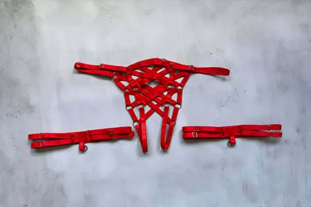 Red Strappy Body Cage Harness and Detached Leg Bands Lay Flat on Grey Background