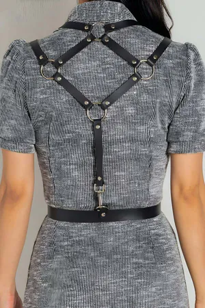 Black faux leather adjustable body harness belt with silver buckle worn over a grey dress